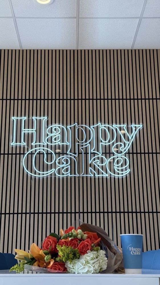 HappyCake neon sign over the counter, with a fresh flower bouquet and a branded coffee cup